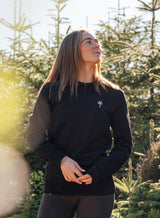Woman wearing a Sutsu Palm Tree EMB Slim Fit Sweatshirt - a black pullover sweatshirt with small embroidered palm tree and sun logo.