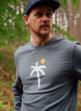Man dressed in a Sutsu Palm Trees Slim Fit Sweatshirt - an organic cotton graphic sweatshirt in grey with a palm tree and sun design.