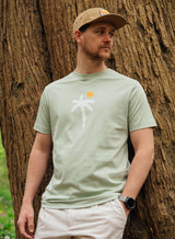 Man wearing a Sutsu Palm Tree T-Shirt - a light green organic cotton t-shirt with printed palm tree and sun graphic.