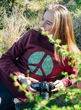 Woman wearing a wine red Sutsu Peace Out Sweatshirt - an organic cotton, graphic sweatshirt with peace symbol and green leaf design.
