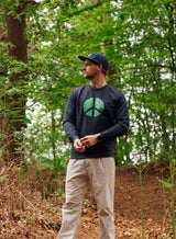 Man wearing a black Sutsu Peace Out Sweatshirt - an organic cotton, graphic sweatshirt with peace symbol and green leaf design.