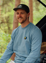 Man wearing a light blue Sutsu Simon Says Peace EMB Sweatshirt - organic cotton sweatshirts with embroidered multi-coloured peace symbol.
