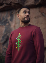 Man in a burgundy Sutsu Xmas Tree Slim Fit Sweatshirt - crew neck festive sweatshirts decorated with tree and colourful baubles.