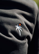 Embroidery detail of a Sutsu Palm Tree EMB Slim Fit Sweatshirt - a black pullover sweatshirt with small embroidered palm tree and sun logo.