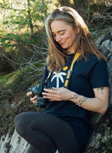 Woman in a rural setting dressed in a Sutsu Palm Tree T-Shirt - a navy organic cotton t-shirt with printed palm tree and sun graphic.