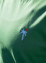 Close up of the design on a Sutsu Palm Tree EMB T-Shirt - a green graphic t-shirt with small embroidered palm tree and sun logo.