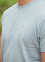 Close up of the design on a Sutsu Palm Tree EMB T-Shirt - a blue graphic t-shirt with small embroidered palm tree and sun logo.