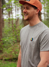 Man wearing a grey Sutsu Simon Says Peace EMB T-Shirt - an organic cotton shirt with embroidered multi-colour peace symbol.
