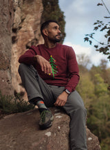 Man in a burgundy Sutsu Xmas Tree Slim Fit sweatshirt with rocks and sky in the background.